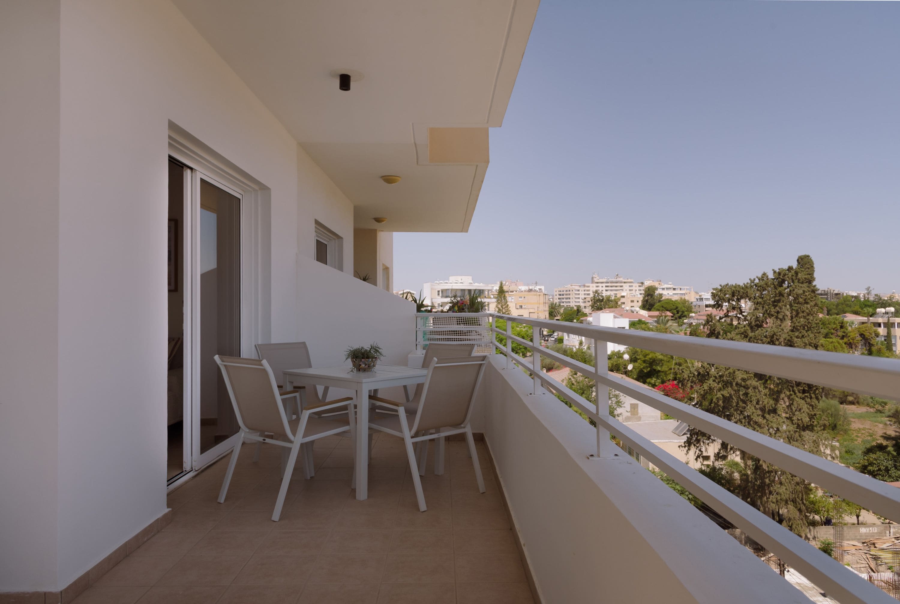 Un balcon avec une table et des chaises, une vue sur le paysage urbain et une porte donnant sur l’intérieur.