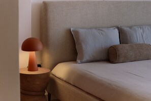A bed with a headboard, pillows, and a bedside lamp on a wooden nightstand. - 160 LCA - Stay Sunshine City Apartment (Larnaca)