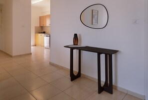 Een hal met een donker houten tafel, een lijst met een foto aan de muur, en een keuken in de achtergrond.