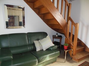 Un canapé en cuir vert, avec une petite table et une plante en pot, placés à côté d’un escalier en bois.