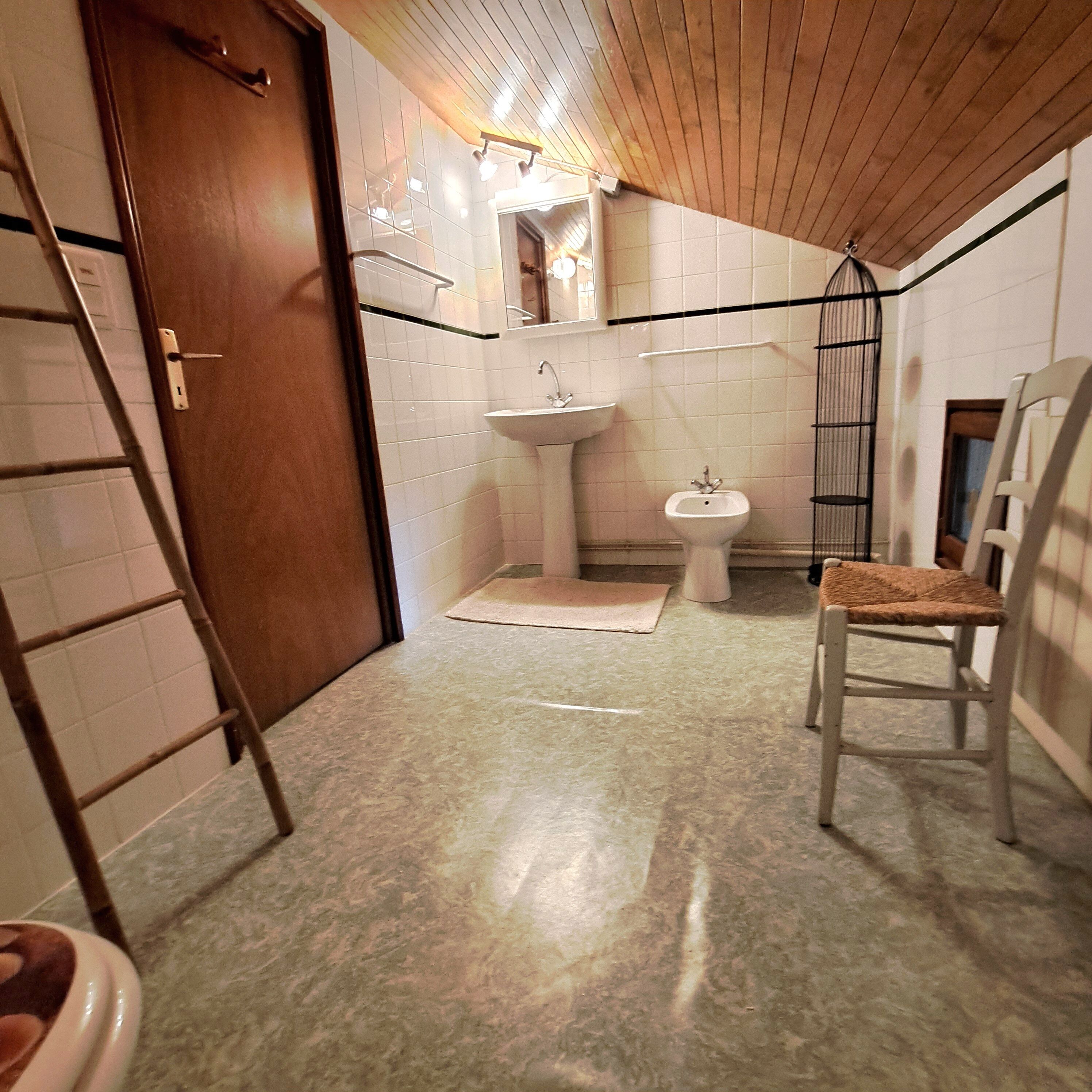 Un bagno con una porta in legno, un lavandino, un bidet, una sedia e una scala.