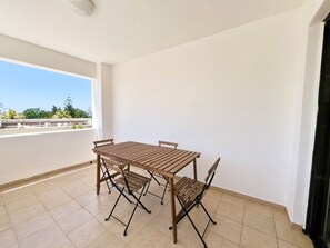A balcony with a wooden table and chairs, a tiled floor, and a white wall. - 161 AN - Stay Napa Zotiko Apartment (Ayia Napa)