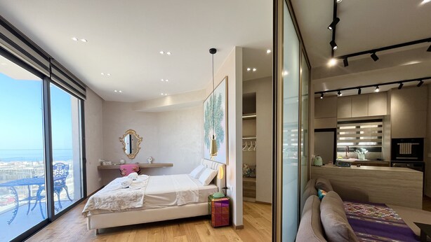 A modern bedroom with a large bed, a sofa, and a view of the city. - 155 PRO - Stay Prime View Apartment (Paralimni)