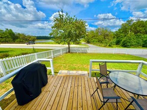 Een houten terras met een tafel en stoelen, een overdekte barbecue en een witte schutting.