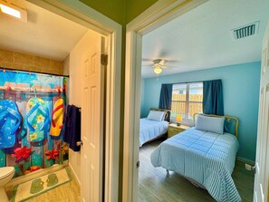 Een kamer met twee bedden, een badkamer met douchegordijn en een raam met gordijnen.