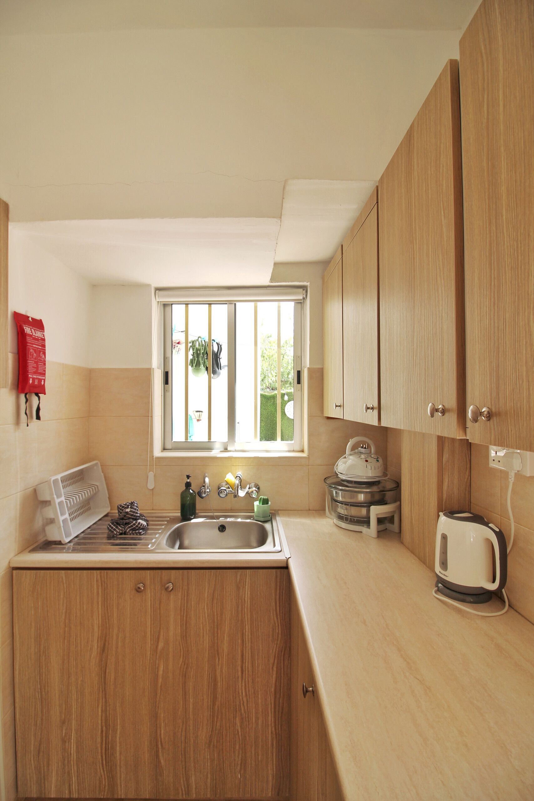 Una cocina pequeña con muebles de madera, un lavamanos, un hervidor y una ventana con vistas a la vegetación.