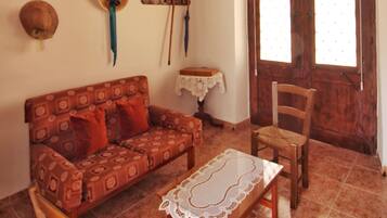 Una sala de estar con techo de madera, un sofá, un sillón, una mesita y un ventanal con cortinas.