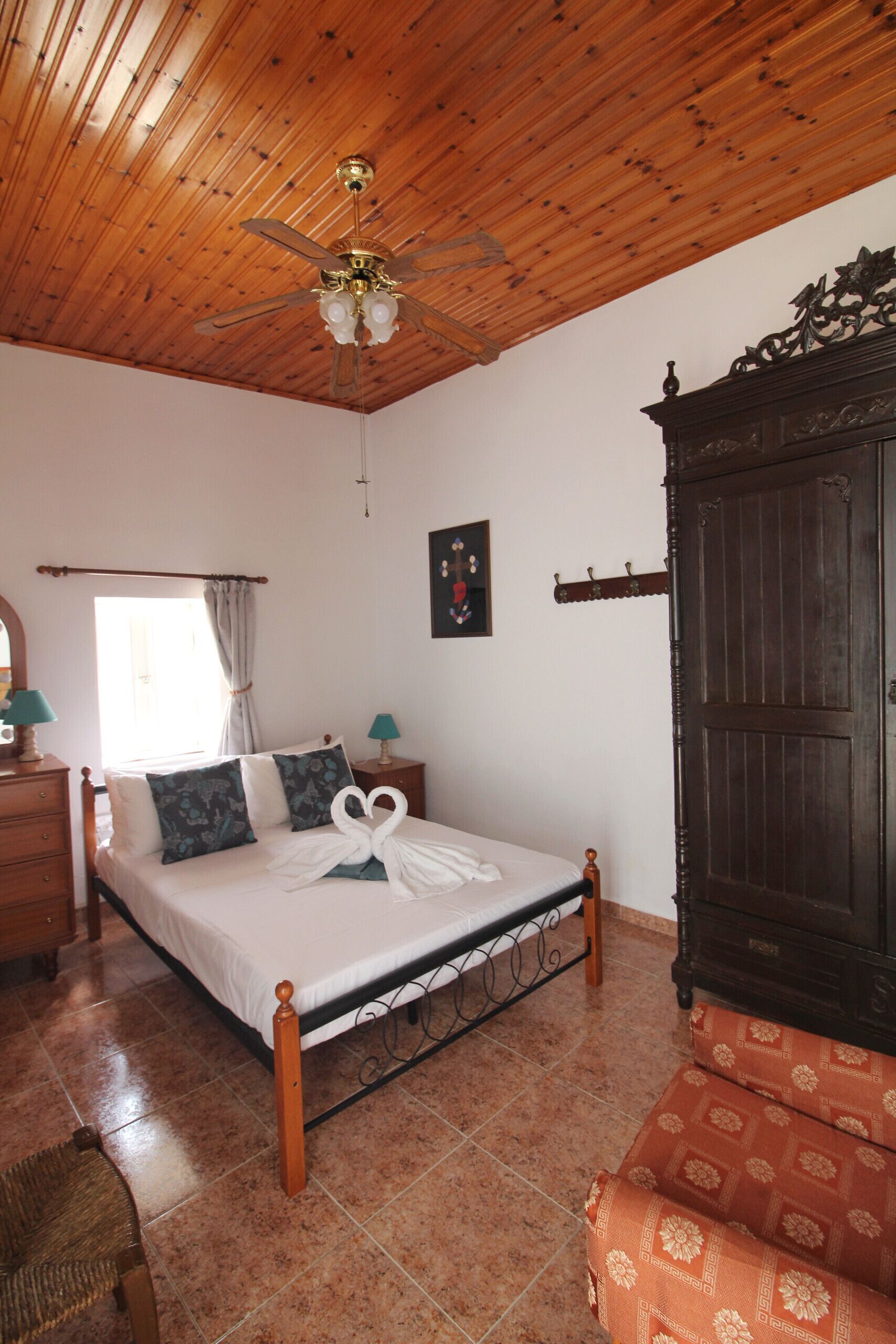 Un dormitorio con techo de madera, una cama con almohada decorada con forma de cisne, un armario y una ventana con cortinas.