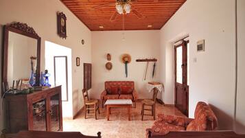 Una habitación con techo de madera, un sofá, una mesa, sillas, un espejo y un perchero en la pared.