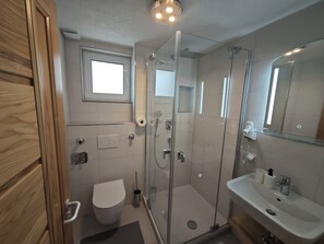 A modern bathroom with a glass-enclosed shower, a toilet, a sink, and a mirror. - Vrbo Property (Reutlingen)