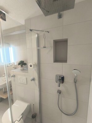 A modern bathroom with a glass shower enclosure, a handheld showerhead, a wall-mounted faucet, and a toilet. - Vrbo Property (Reutlingen)