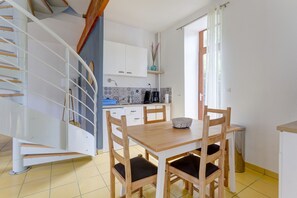 A kitchen with a dining table and chairs, a staircase, and a window with curtains. - La Dorine - Charmant cocon pour 2 en campagne (Parfondeval)