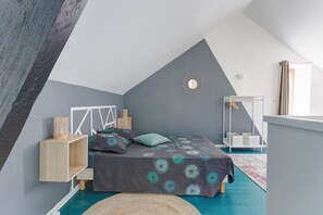 Un dormitorio con techo inclinado, una cama con colcha estampada, una mesita de noche con cesta y una lámpara colgante.
