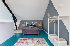 A bedroom with a sloped ceiling, a bed with a headboard, a bedside table, a hanging light fixture, a wardrobe, and a floor lamp. - La Dorine - Charmant cocon pour 2 en campagne (Parfondeval)