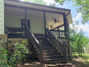 A covered porch with a staircase leading to a second level, stone walls, and a ceiling fan. - The Lookout at Lakeshore Estates (Hardin County)