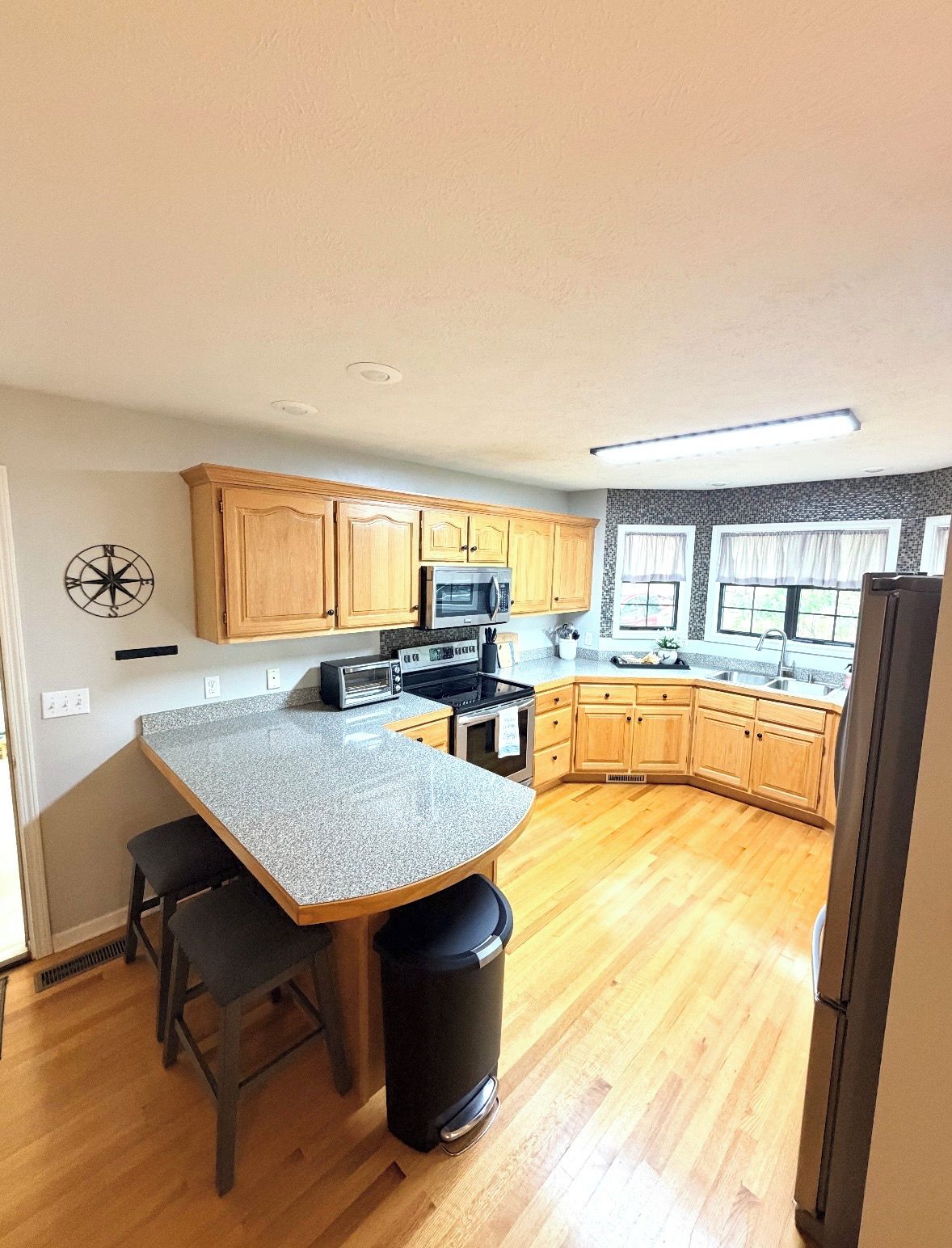 A kitchen with wooden cabinets, a granite countertop, a microwave, a stove, and a trash can.
