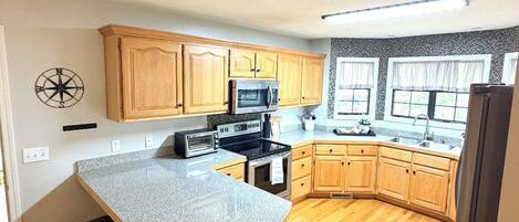 Une cuisine avec des meubles en bois, un plan de travail en granit, un four à micro-ondes, une cuisinière et une poubelle.