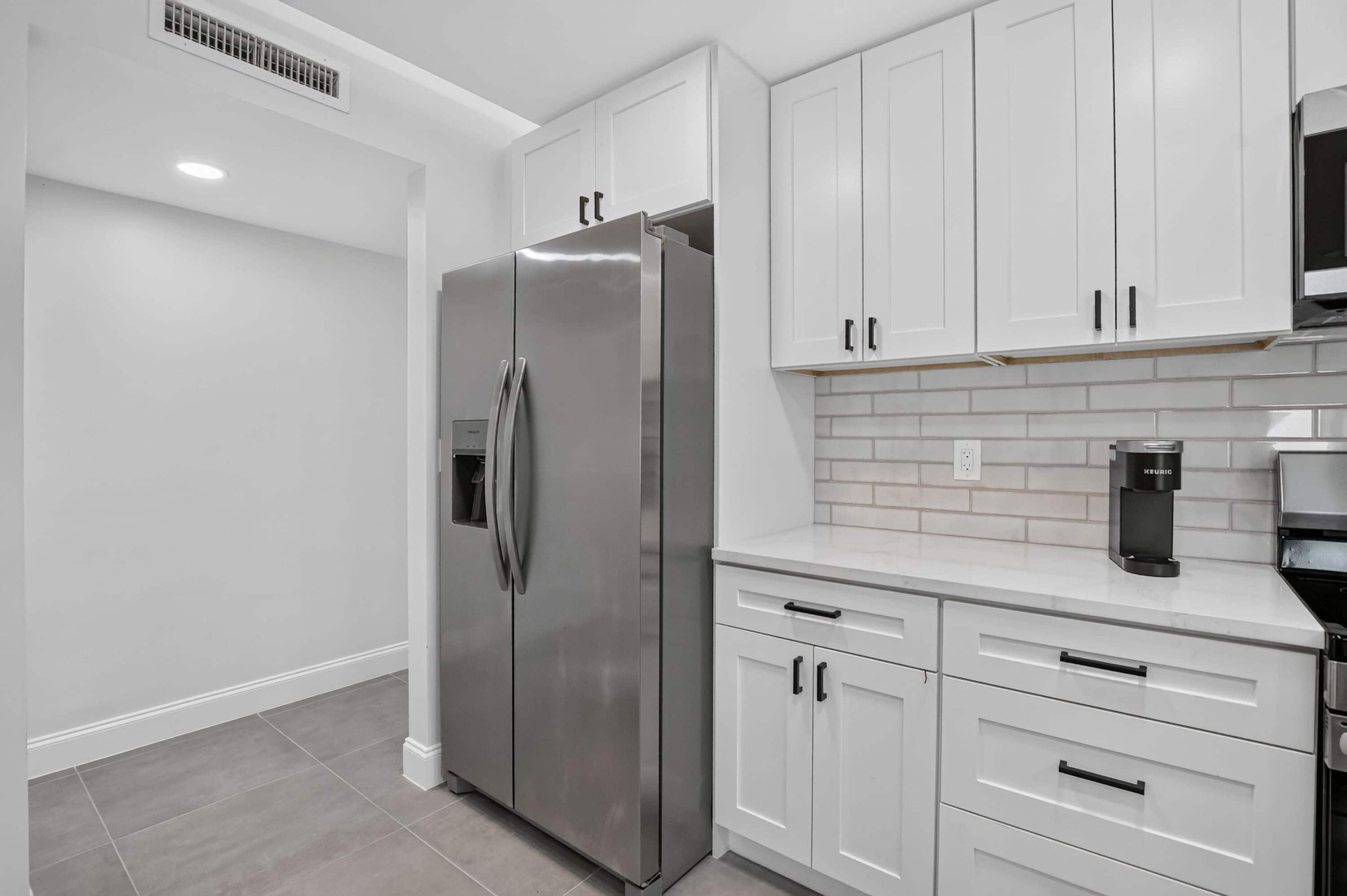 Una cocina moderna con refrigerador de acero inoxidable, armarios blancos y salpicadero de azulejos.