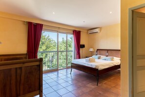A bedroom with a bed, a window with curtains, an air conditioning unit, and a view of greenery outside. - Villa Occitane La Roche de Glun (La Roche-de-Glun)