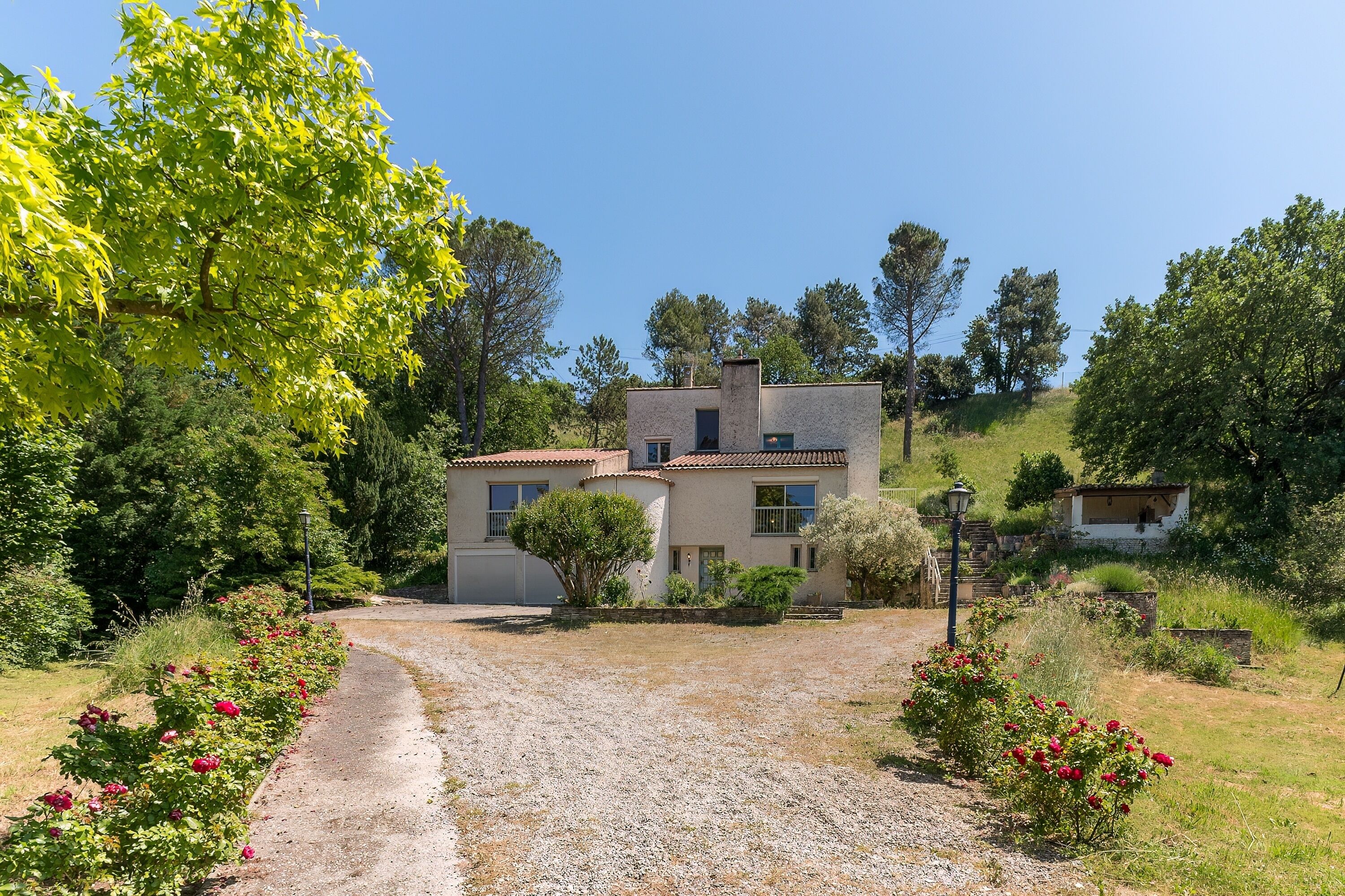 A two-story house with a gravel driveway and a garden with red flowers.