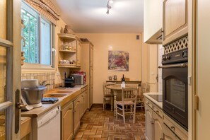 A compact kitchen with a built-in oven, a dining table with chairs, and a window with curtains. - Villa Occitane La Roche de Glun (La Roche-de-Glun)