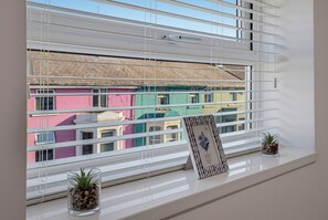 A window with horizontal blinds, a framed picture, and two small potted plants on a windowsill. - The Tide Apartments (Blackpool)