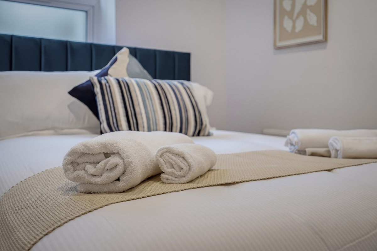 A neatly made bed with rolled towels and a striped pillow.