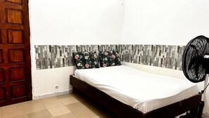 Ein Schlafzimmer mit einem Bett, einer Holztür, einer Wand mit Steinmusterung und einem Standventilator.