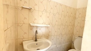 Ein Badezimmer mit Waschbecken, Toilette und einem kleinen Regal darüber.