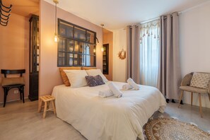 A hotel room with a large bed, a wooden chair, a small stool, and a window with curtains. - The White Forest - Proche Epinal (Thaon-les-Vosges)