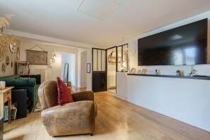 Un salon avec un grand téléviseur à écran plat fixé au mur, un canapé vert, un fauteuil marron et une table basse en bois.