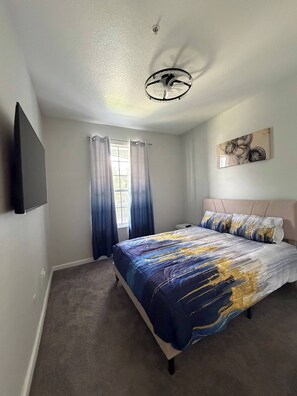 A bedroom with a bed, a ceiling fan, a window with curtains, and a wall-mounted TV. - Beautiful Apartment near Disney (Kissimmee)