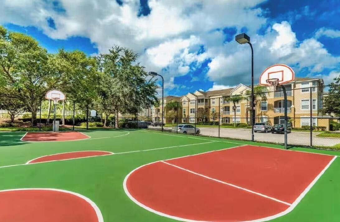 An outdoor basketball court with a clear sky and residential buildings in the background.