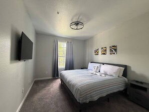 Ein Schlafzimmer mit einem Bett, einem Flachbildfernseher, einem Deckenventilator und Kunstwerken an der Wand.