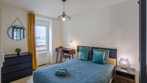 Quarto com cama, escrivaninha, cadeira, cômoda, espelho e janela com cortinas.