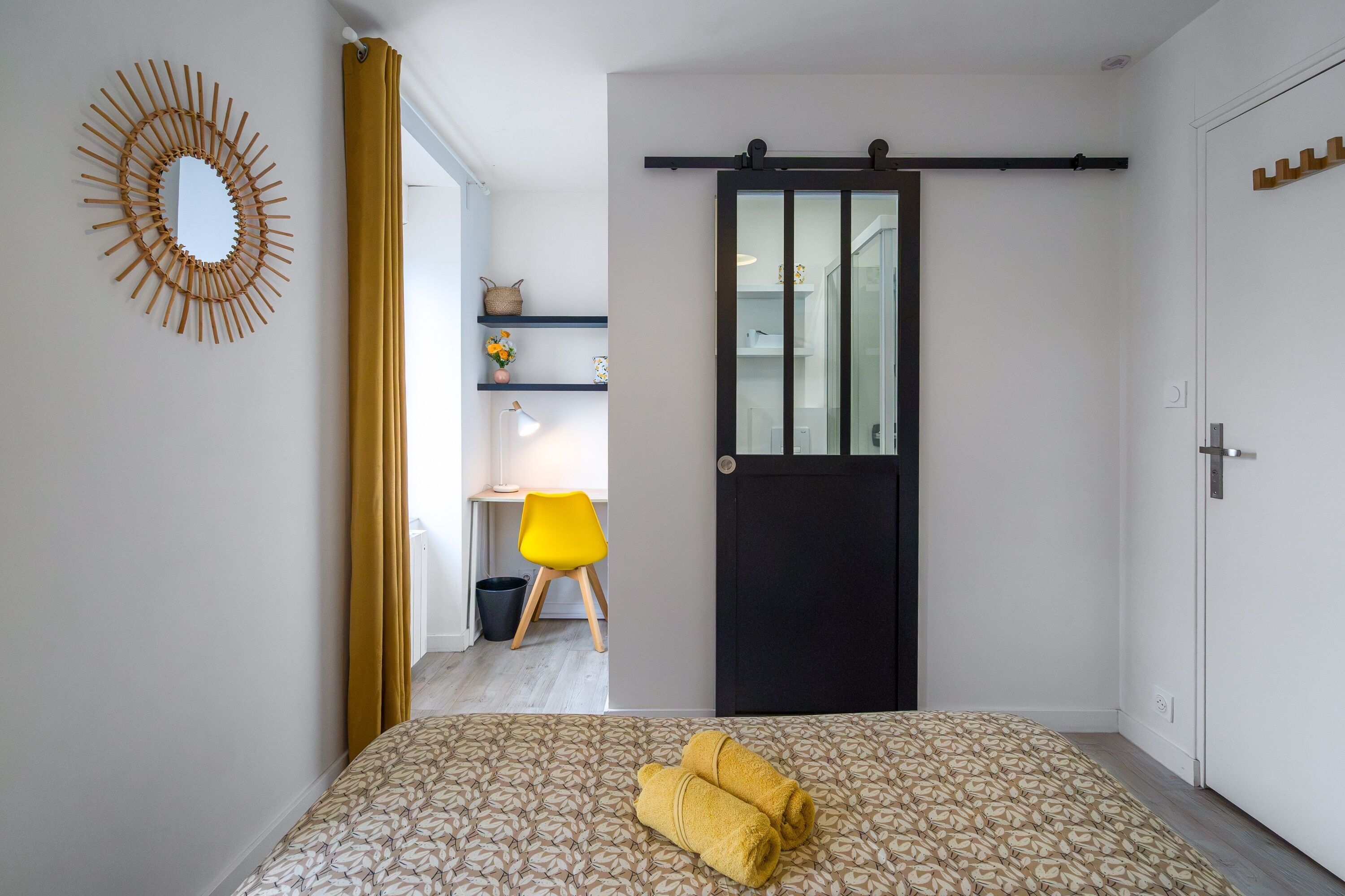 A bedroom with a bed, a desk with a chair, a wardrobe, and a bathroom visible through a sliding door.