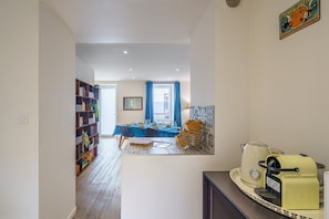Eine moderne Küche mit einer Kaffeemaschine, ein Essbereich mit einem Tisch für zwei Personen und eine Bücherwand voller Bücher.