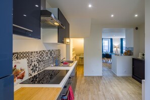Une cuisine moderne avec un revêtement mural noir et blanc, un îlot central et un coin repas visible à travers une porte ouverte.