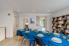 A dining area with a long table set for six, surrounded by chairs, with a bookshelf filled with books to the right. - Ti Donnart - 10min du Centre de Brest (Brest)