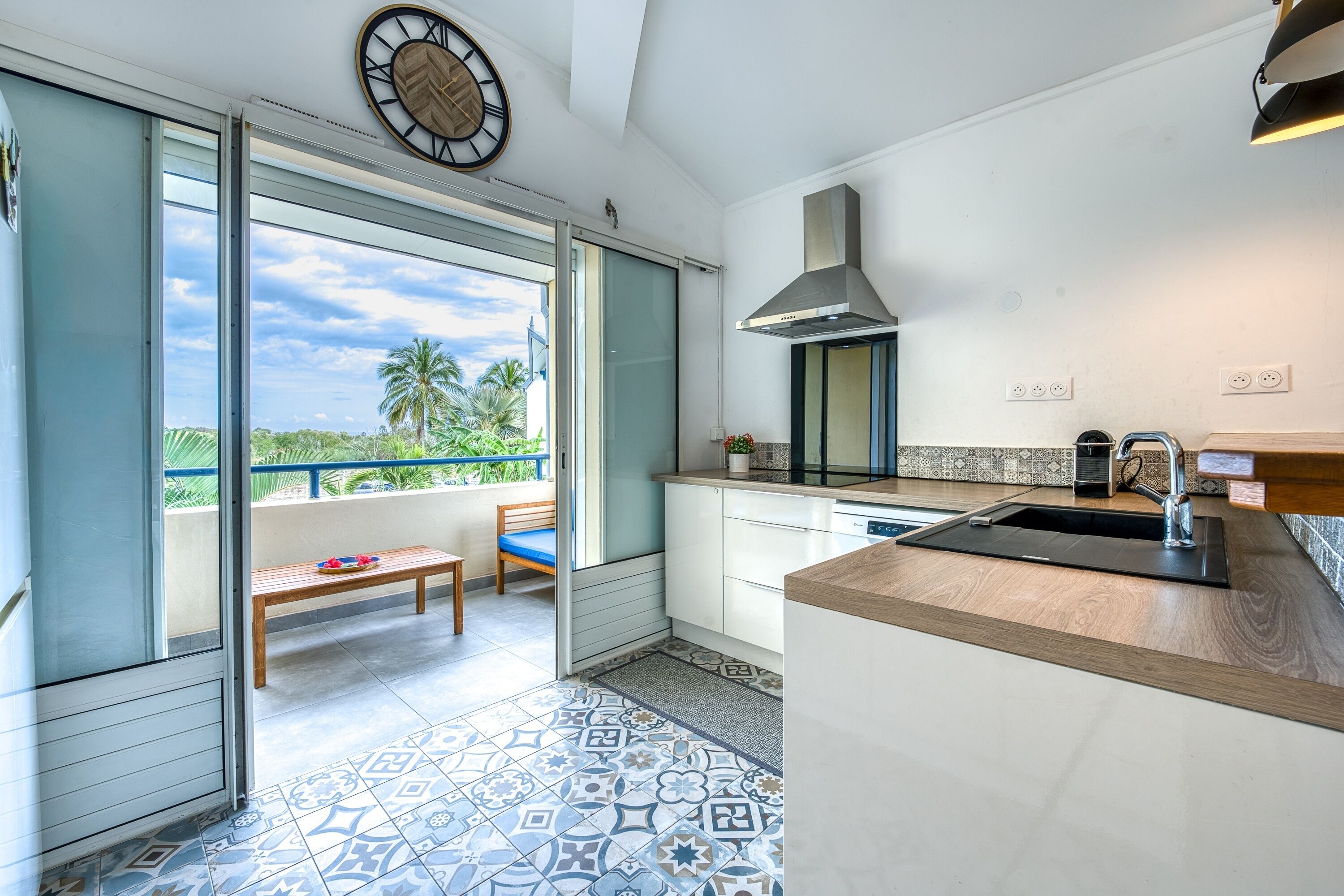 A modern kitchen with a large window, a dining area with a bench, and a view of palm trees.