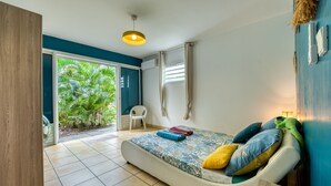 Quarto com cama, uma cadeira, janela e porta que dá para uma varanda.