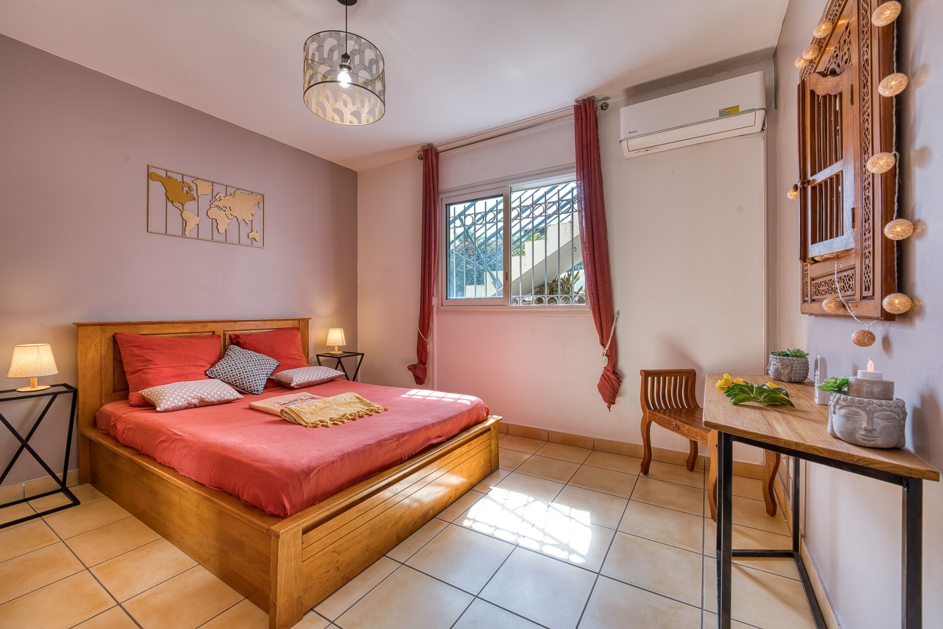 Een slaapkamer met een houten bed, een nachtkastje met een lamp, een raam met gordijnen en een wandairconditioner.