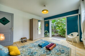 Ein Zimmer mit einer großen Schiebeglastür, die zu einem Garten führt, einem Sofa mit einem gemusterten Teppich, einem kleinen Tisch und einer hängenden Leuchte.
