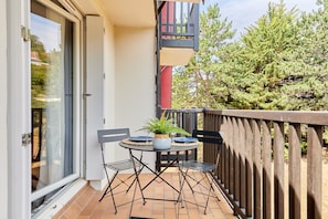A small outdoor balcony with a table and chairs, a potted plant, and a view of trees and a building. - Cocon Entre Mer, Nature et Histoire (Blonville-sur-Mer)