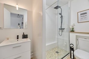 A modern bathroom with a glass-enclosed shower, white tiles, a white sink, and a framed sign on the wall. - Cocon Entre Mer, Nature et Histoire (Blonville-sur-Mer)