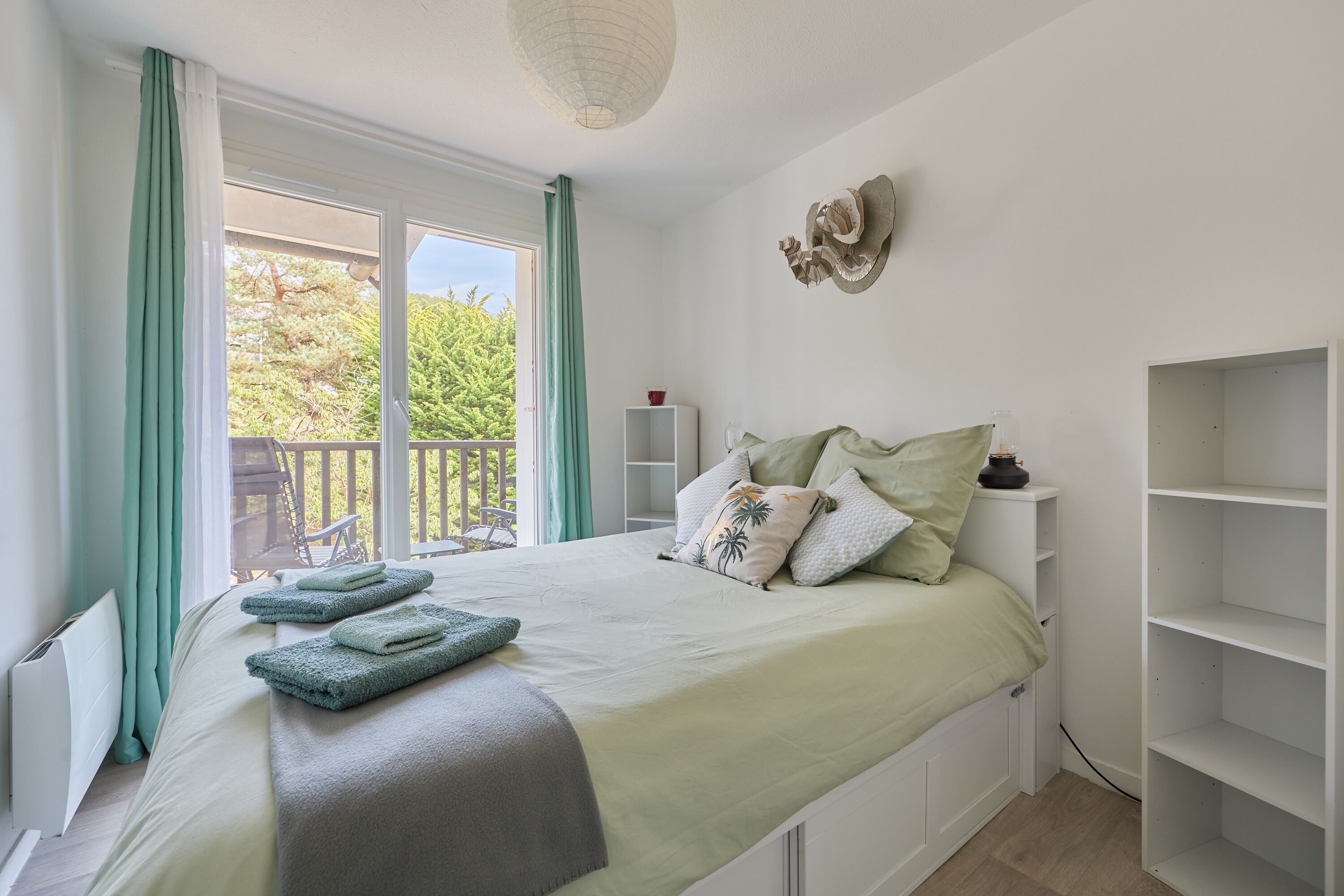 Un dormitorio con cama, ventana, balcón y estante de pared.