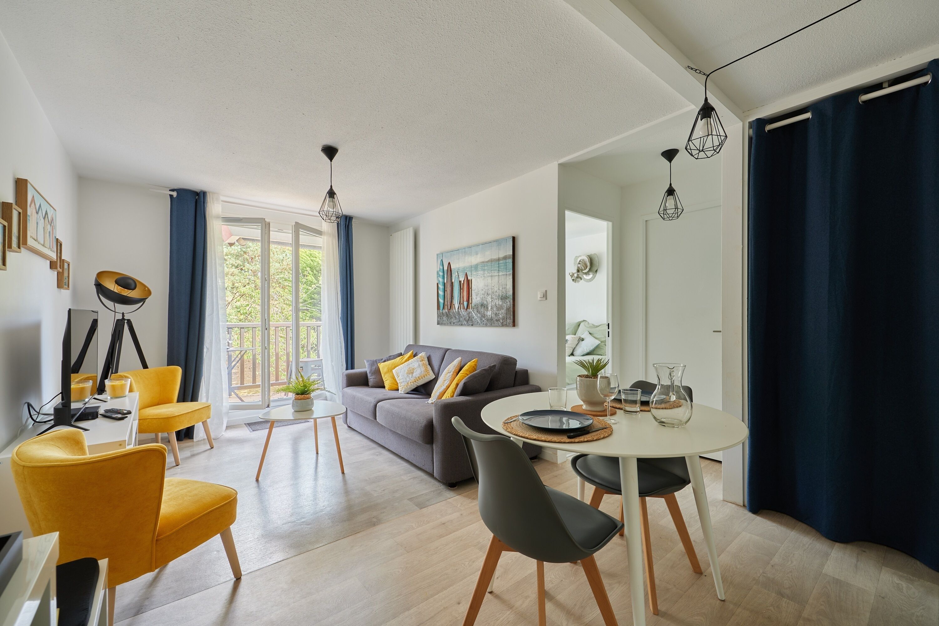 Una sala de estar moderna con sofá, sillas amarillas, una mesa de comedor con sillas y un ventanal con cortinas.