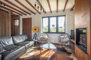 A living room with a leather sofa, two chairs, a small table, a floor lamp, and a television. - Beach house Sainte-Cécile - Avec beau jardin (Camiers)