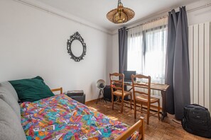 A bedroom with a bed, a desk, a chair, a lamp, and a window with curtains. - Beach house Sainte-Cécile - Avec beau jardin (Camiers)