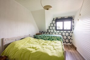 Ein Schlafzimmer mit schrägen Wänden, einem Fenster mit floralem Muster und einem Bett mit grüner Bettdecke.